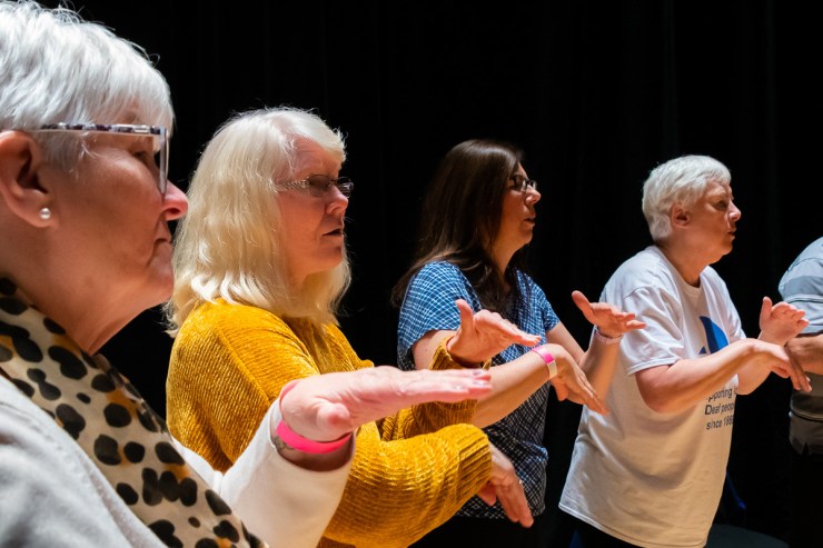 four people in bright coloured clothes using British Sign Language.